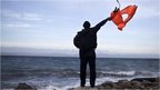 A local man uses a discarded life jacket to signal to an incoming rubber boat filled with migrants and refugees at a beach on the northern coast of Lesbos, Greece