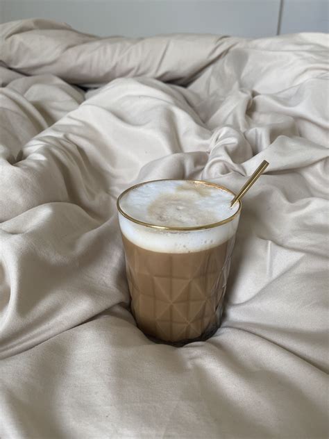 a cup of coffee sitting on top of a bed covered in white sheets with a ...