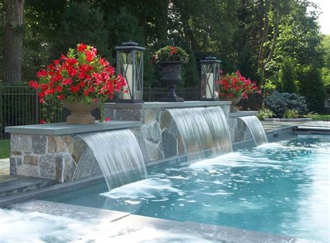 an outdoor pool with waterfall and red flowers