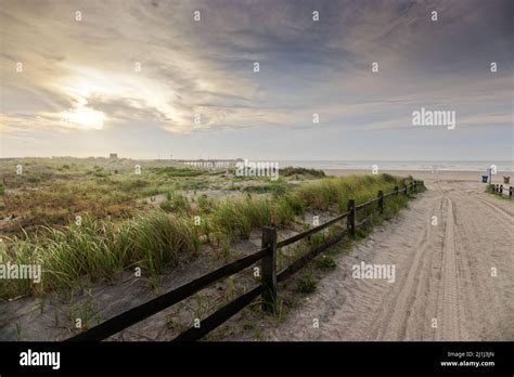 A scenic shot of a sand road leading to a beach and the grass field on ...