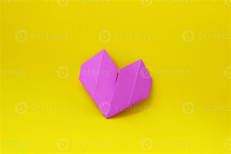 Purple paper origami heart on a yellow background in the center of the ...