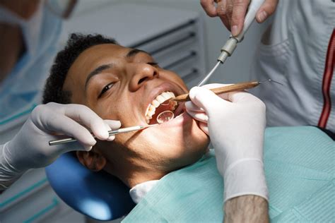 cleanings Dentist examining oral cavity of young African-American man ...