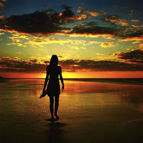 a woman standing on top of a beach next to the ocean under a cloudy sky