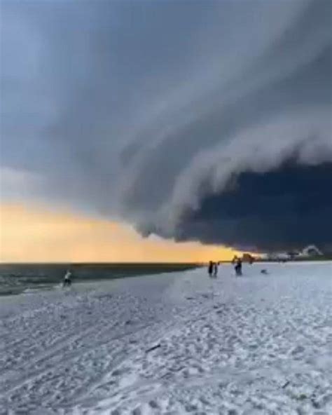 people walking on the beach under a very large storm moving across the ...