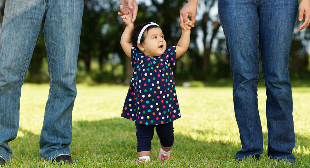 Toddler learning to walk holding her parents hands