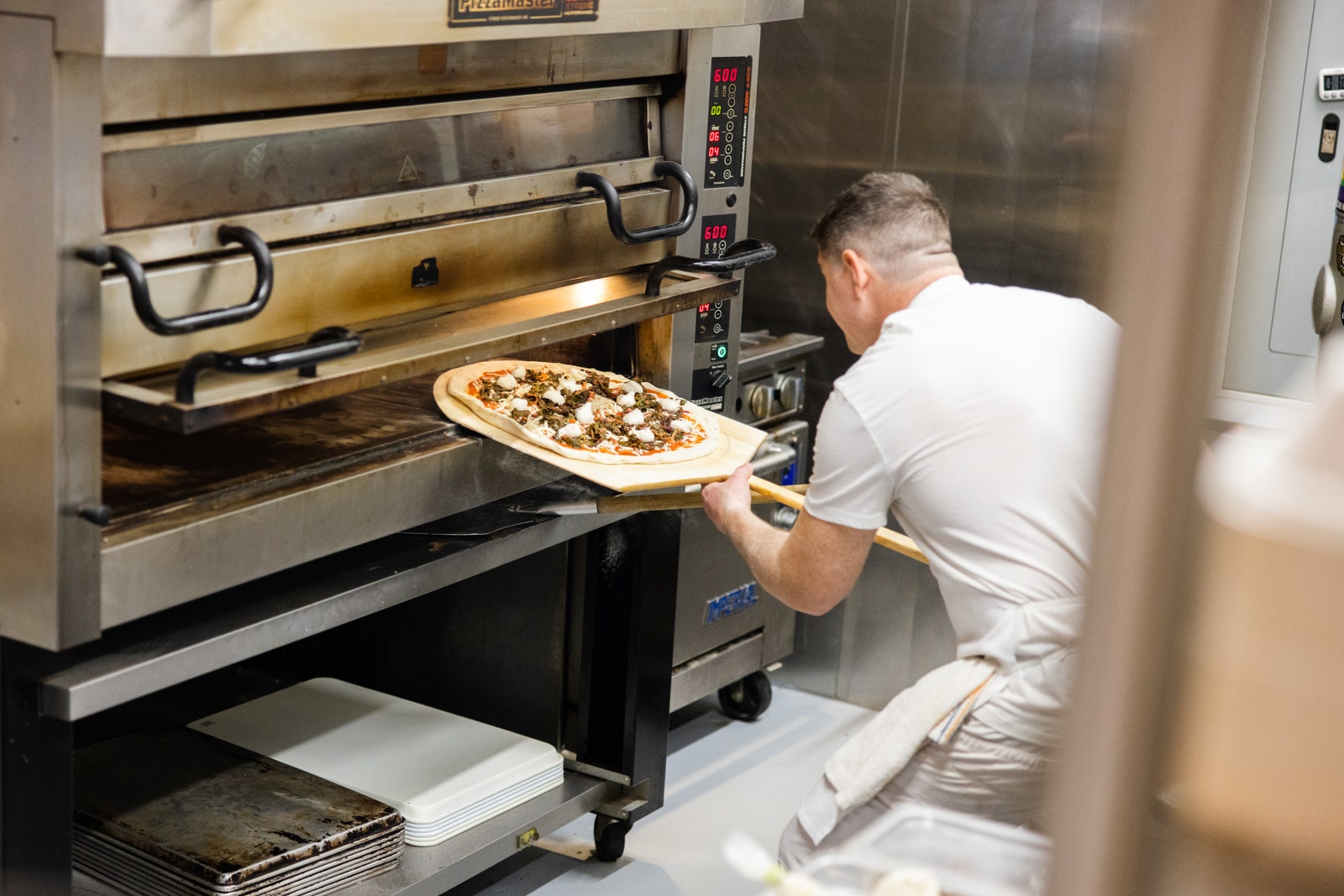 A cook inserting a pizza into a pizza oven.