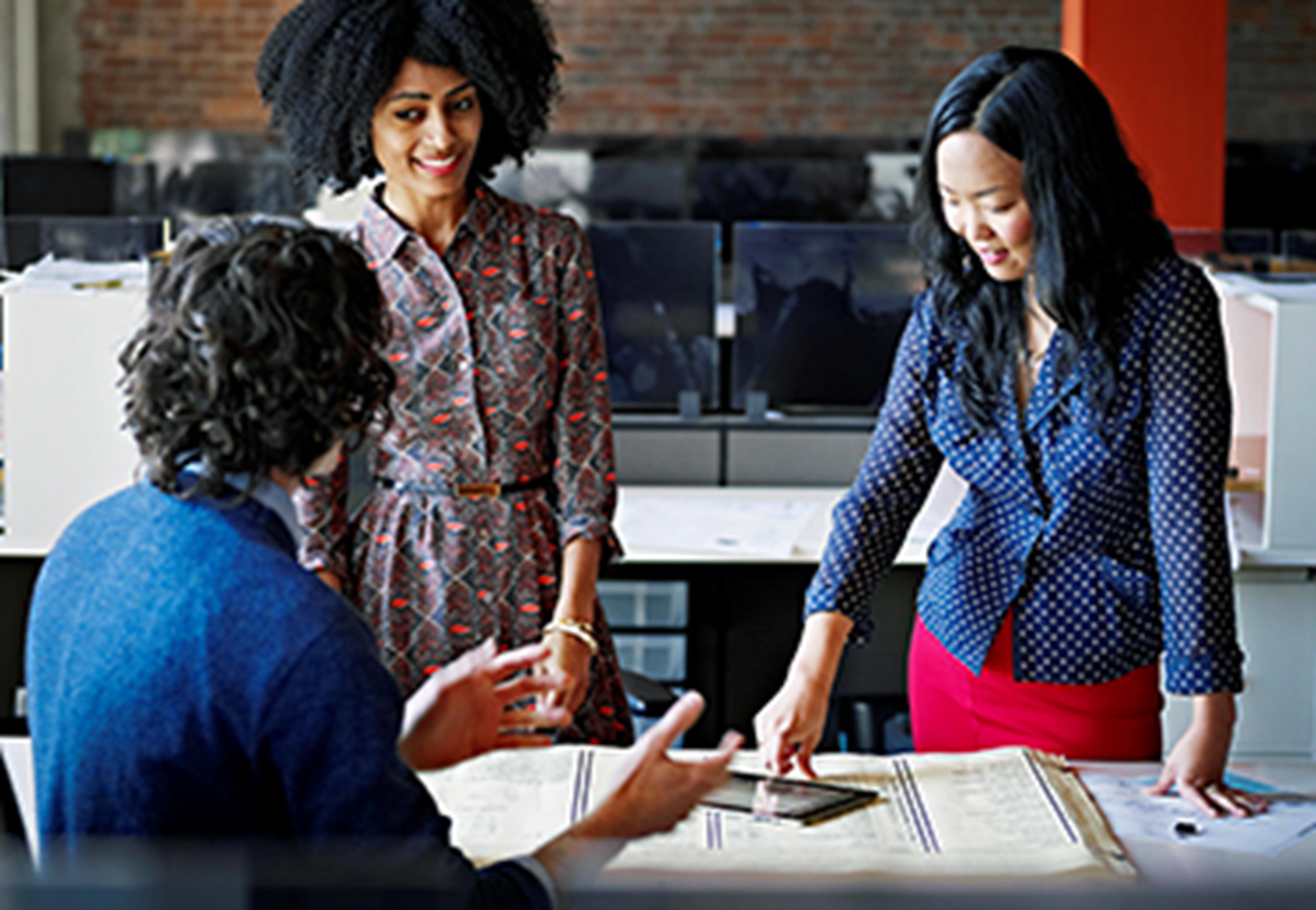 Three people talking and standing around a table with papers