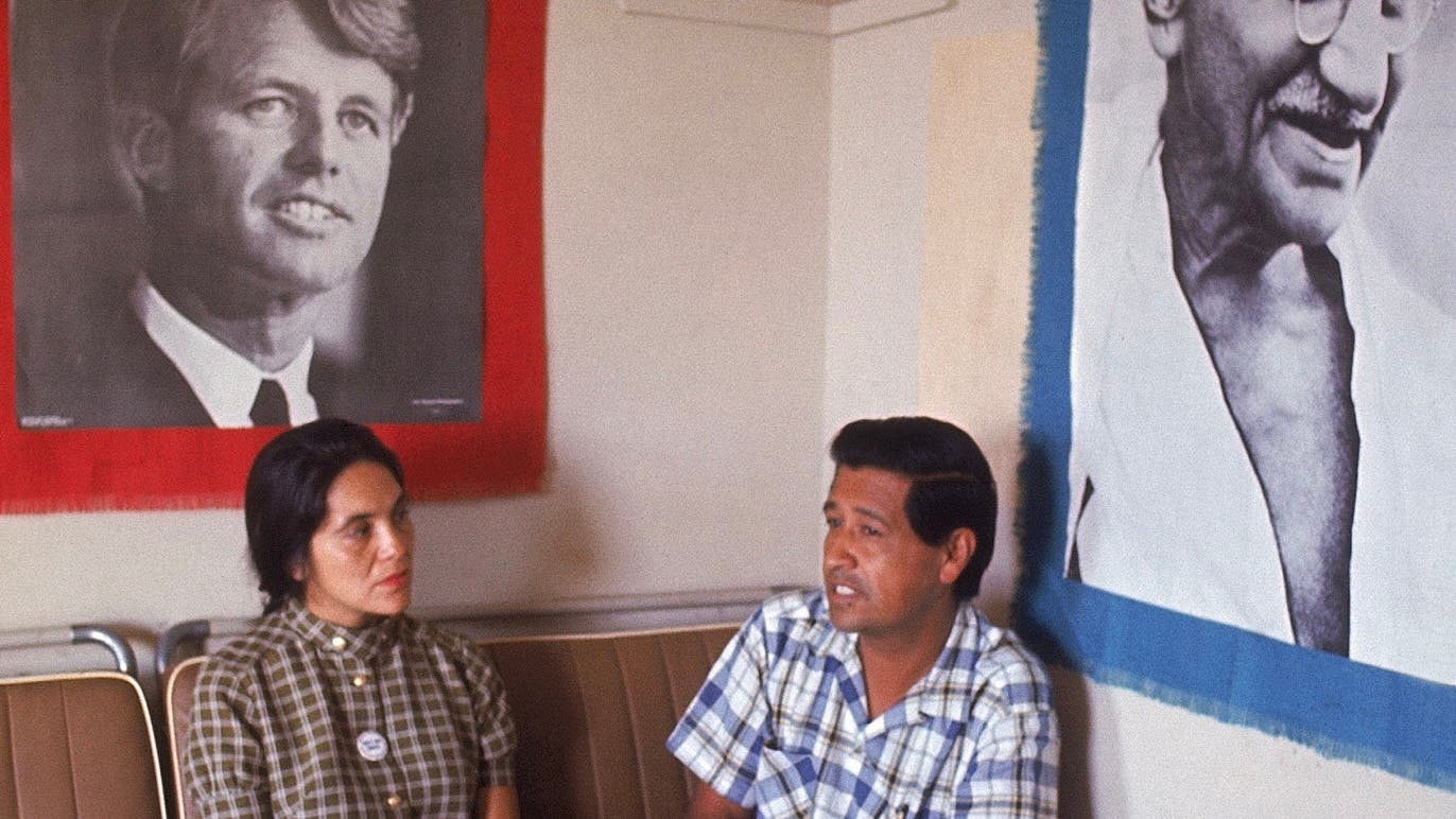 United Farm Workers co-founders Dolores Huerta and Cesar Chavez sit together under portraits of Robert Kennedy and Mahatma Gandhi.