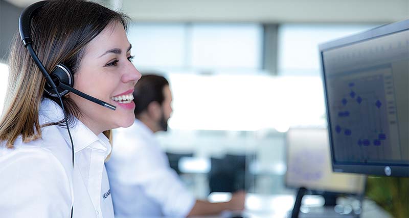 Woman smiling wearing a headset and sitting in front of a computer