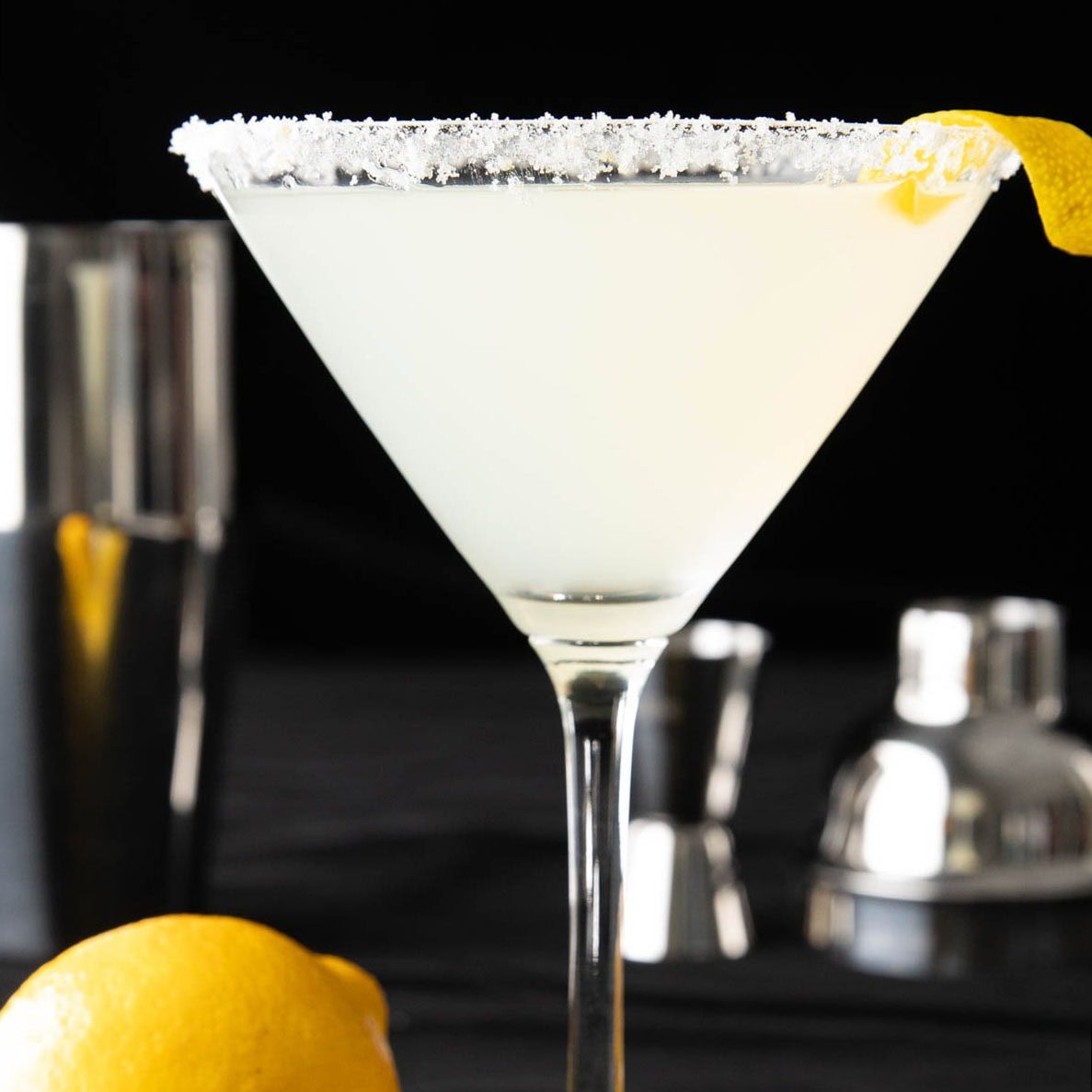 Closeup of lemon drop martini with lemon sugar rim and lemon garnish on a black background.