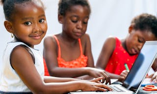 Portrait of cute little African girl doing homework on computer with friends at desk.Isolated on light background.