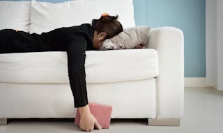 Exhausted, Tired, Lazy, sleepy Asian Business woman in black suit lying on white sofa with blue wall and copy space. Stress from