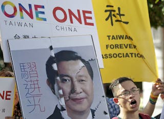 An activist holding a placard showing the merged faces of Taiwan's President Ma and China's President Xi, protests against the u