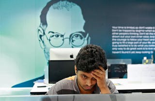 An employee works on a computer terminal against the backdrop of a picture of late Apple co-founder Jobs at the Start-up Village