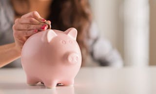 Woman Putting Coin In Piggy Bank, Indoors