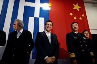 Greek PM Tsipras smiles in front of a Greek national flag and a Chinese national flag before his speech aboard the Chinese friga