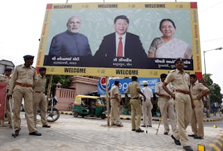 Police personnel stand guard in front of a boarding with images of India's PM Modi, China's President Xi and Patel, Chief Minist