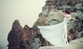 Beautiful bride posing on the coast with angelic dress. Bride in wedding dress stands on a cliff with a beautiful sea view from 