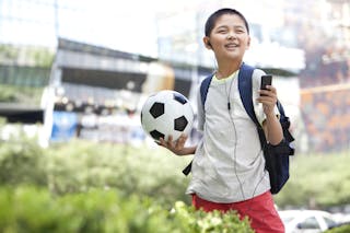 Schoolboy listening to MP3 player with football in hand