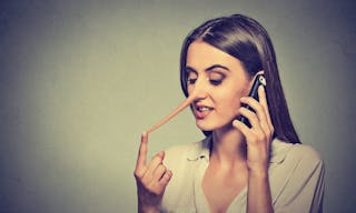 Portrait young woman talking on mobile phone telling lies has a long nose isolated on gray wall background 