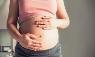 Pregnant woman feeling happy at home while taking care of her child. The young expecting mother holding baby in pregnant belly.