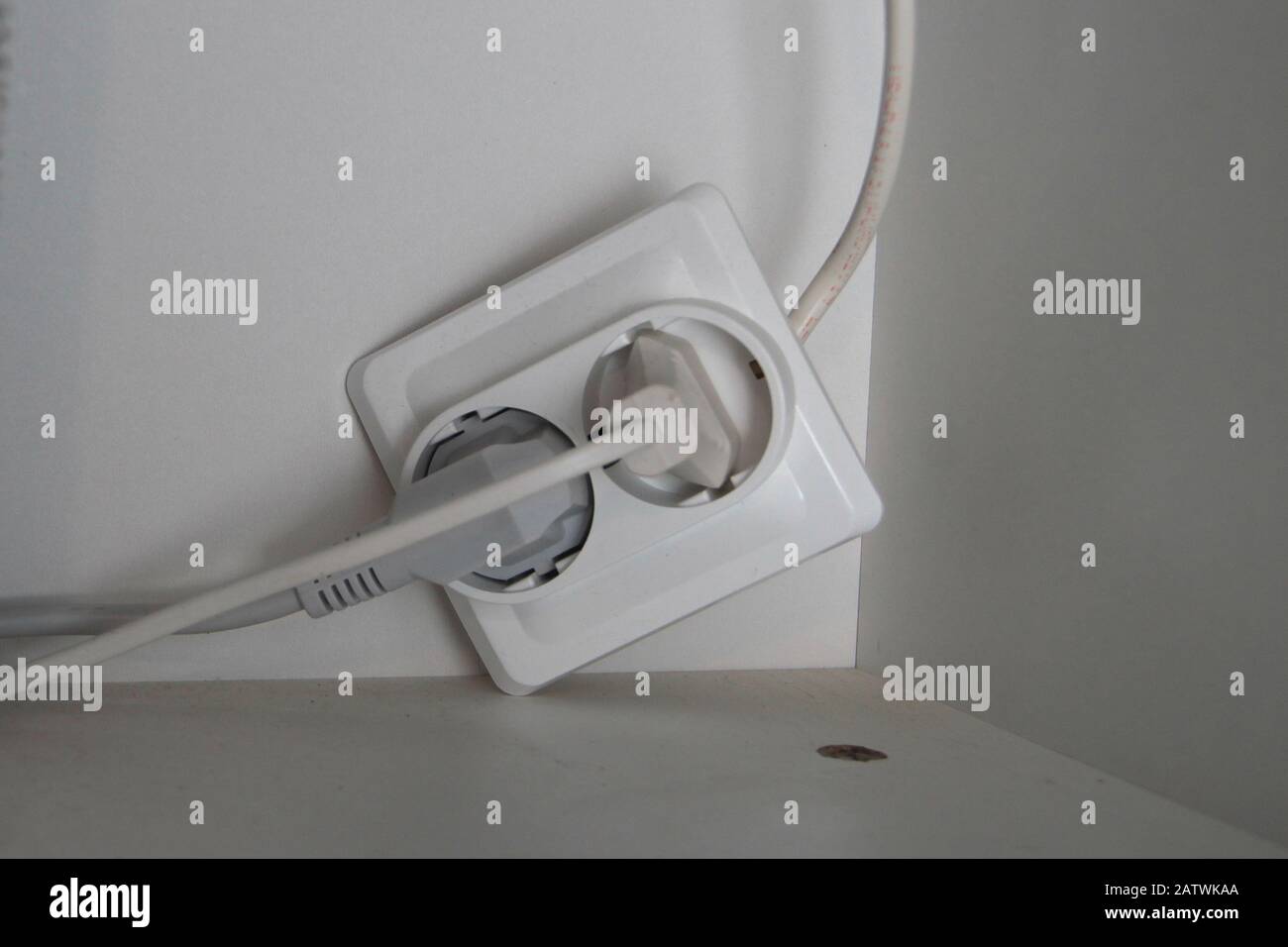 Two electrical plugs are plugged into a broken outlet. Stock Photo