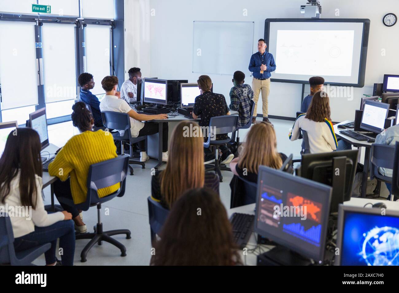 Junior high students at computers watching teacher at projection screen in classroom Stock Photo