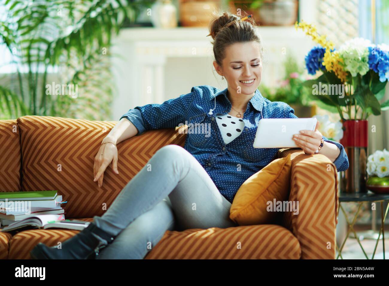 smiling stylish woman in jeans shirt with tablet PC study online in the modern living room in sunny day. Stock Photo