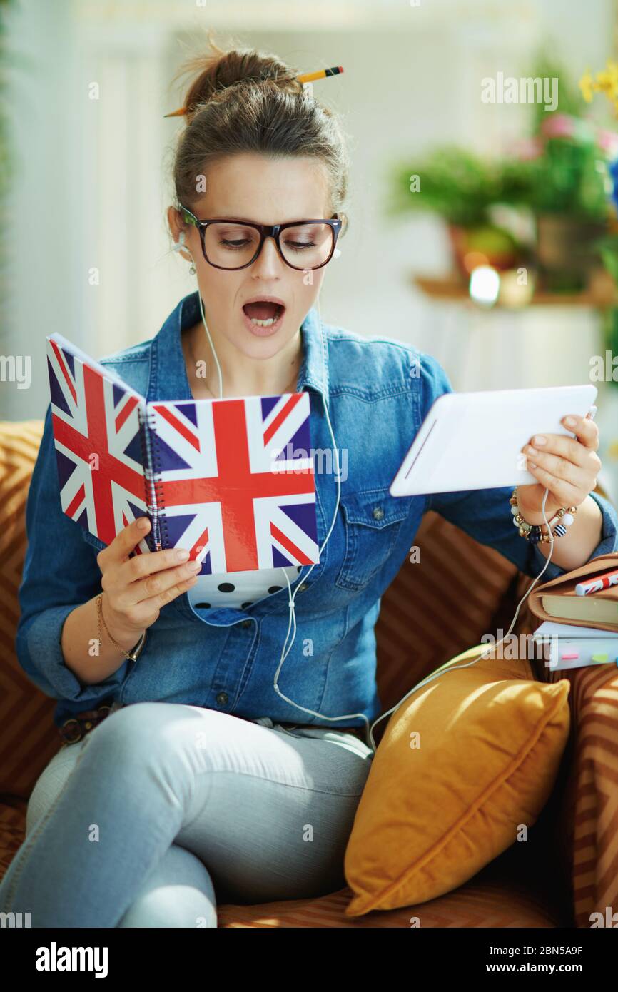 stylish housewife in jeans shirt with tablet PC and UK flag notebook learning foreign language online in the modern house in sunny day. Stock Photo