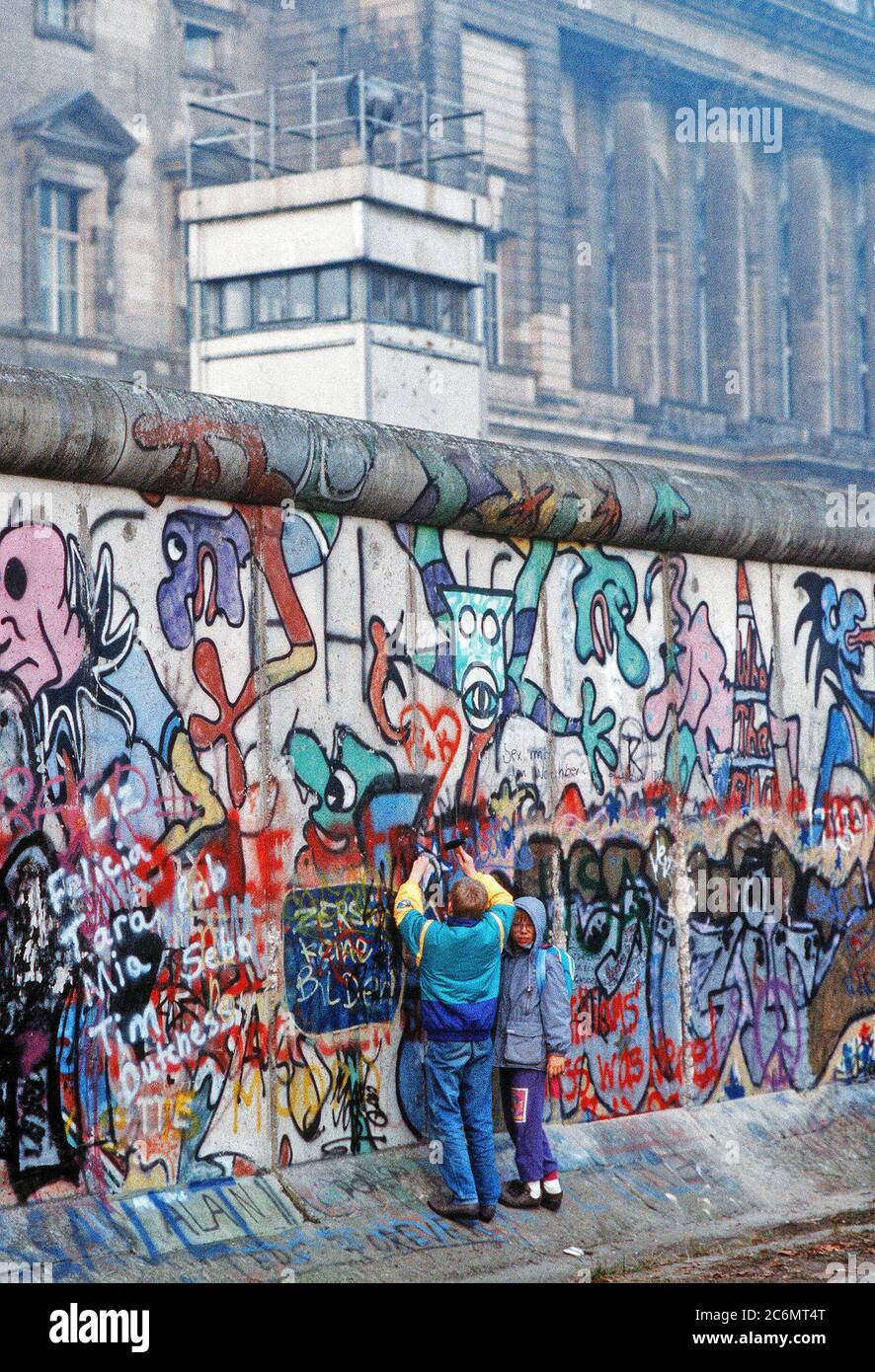 West German children attempt to chip off a piece of the Berlin Wall as a souvenir.  A portion of the Wall has already been demolished at Potsdamer Platz. Stock Photo