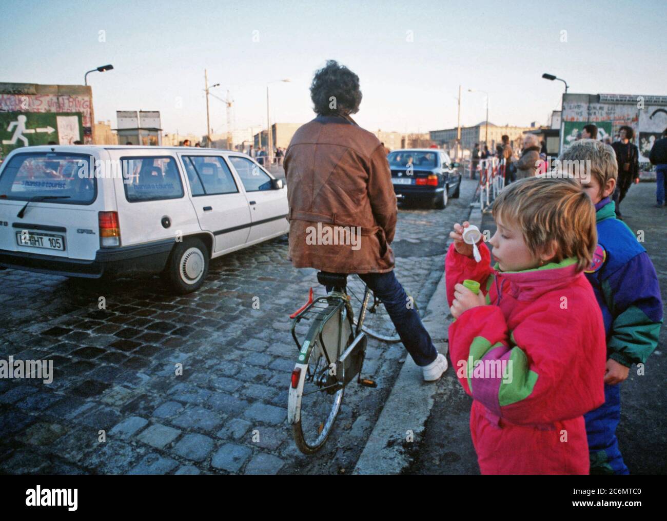 A child blows bubbles at the passing traffic as cars move between East and West Berlin at Potsdamer Platz. Stock Photo