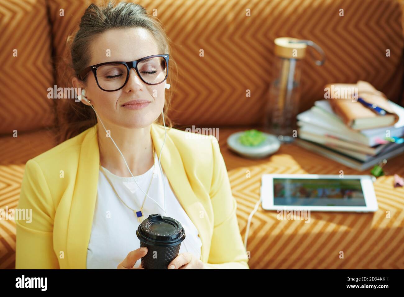 relaxed trendy woman in yellow jacket with coffee cup using online school on a tablet PC at modern home in sunny day. Stock Photo