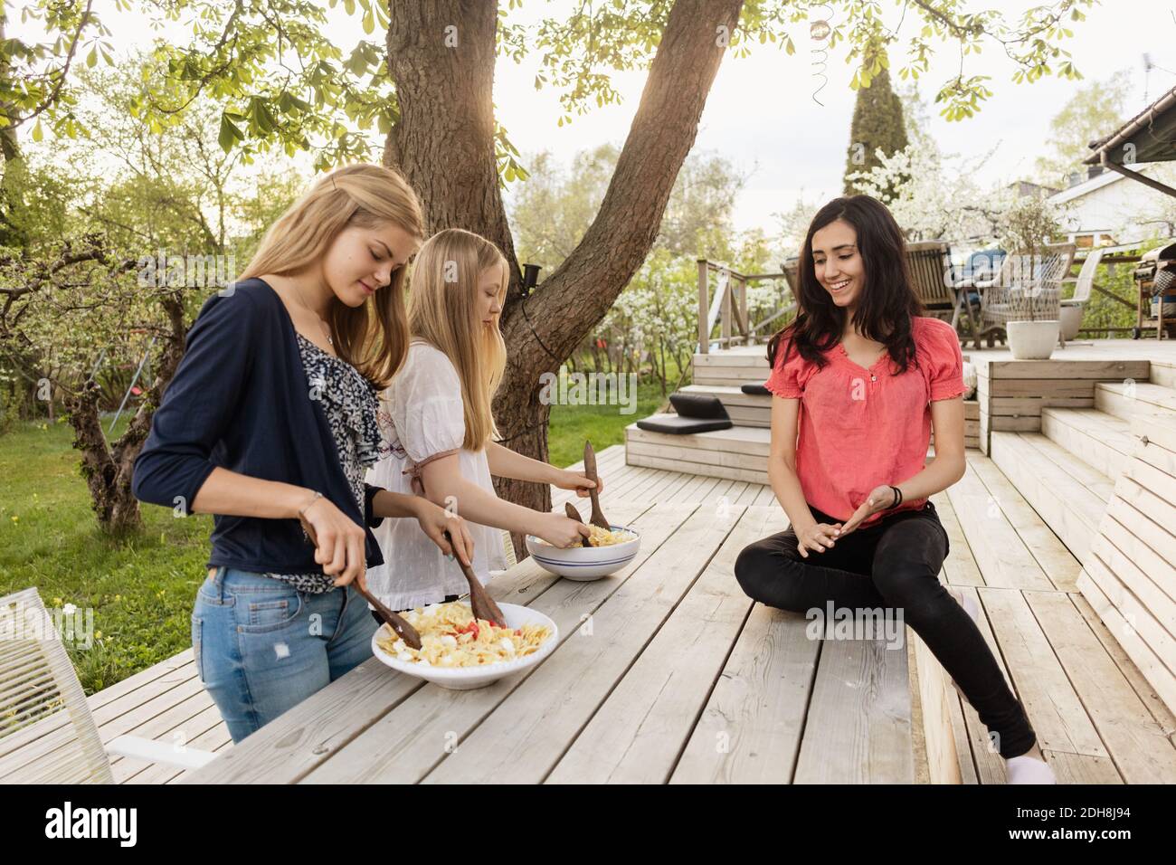 Teenage girls mixing salad at wooden table in yard Stock Photo