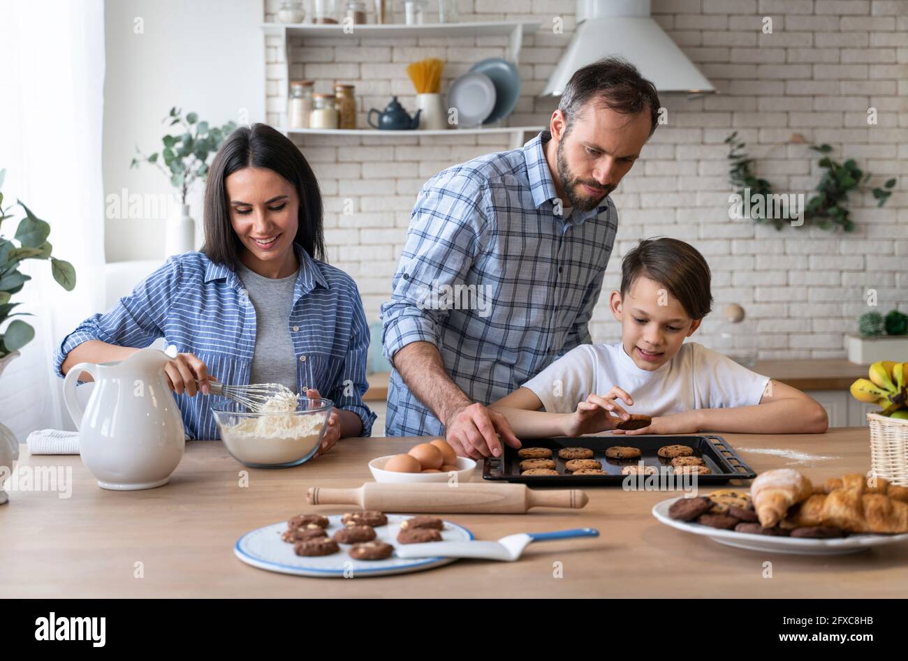 Father and son looking at biscuit while mother mixing flour in kitchen at home Stock Photo