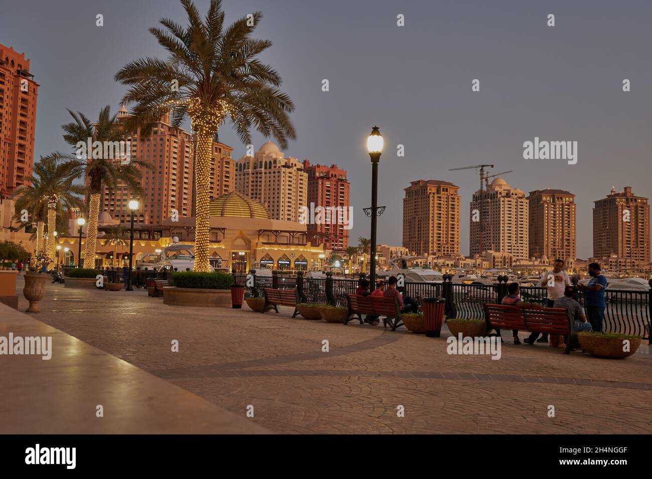 Porto Arabia  in The pearl Doha, Qatar sunset winter shot showing people walking and sitting on promenade with skyline in background Stock Photo