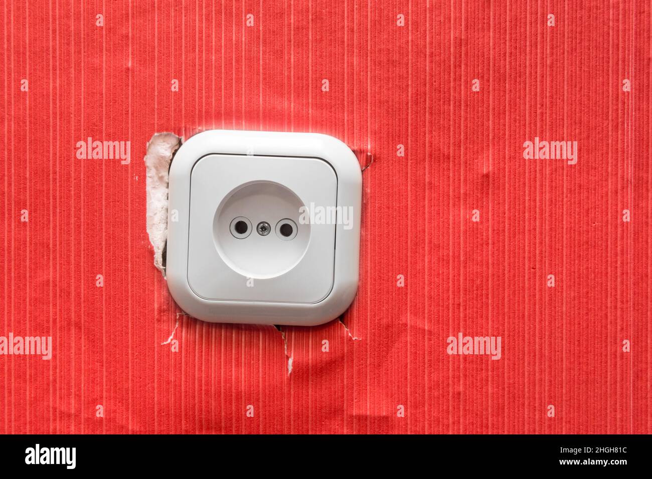 Old broken damaged socket in the wall with red wallpaper, close up. Stock Photo