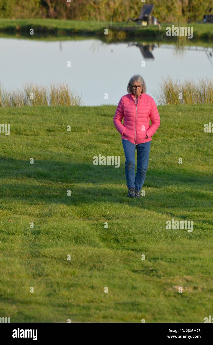 lone older woman, walking near fishing lake kent england Stock Photo