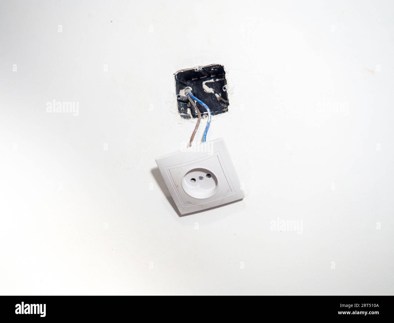 Broken electrical socket on the wall. Disassembled device. White wall with a socket pulled out of the wall. Life threatening. Broken electrical equipm Stock Photo