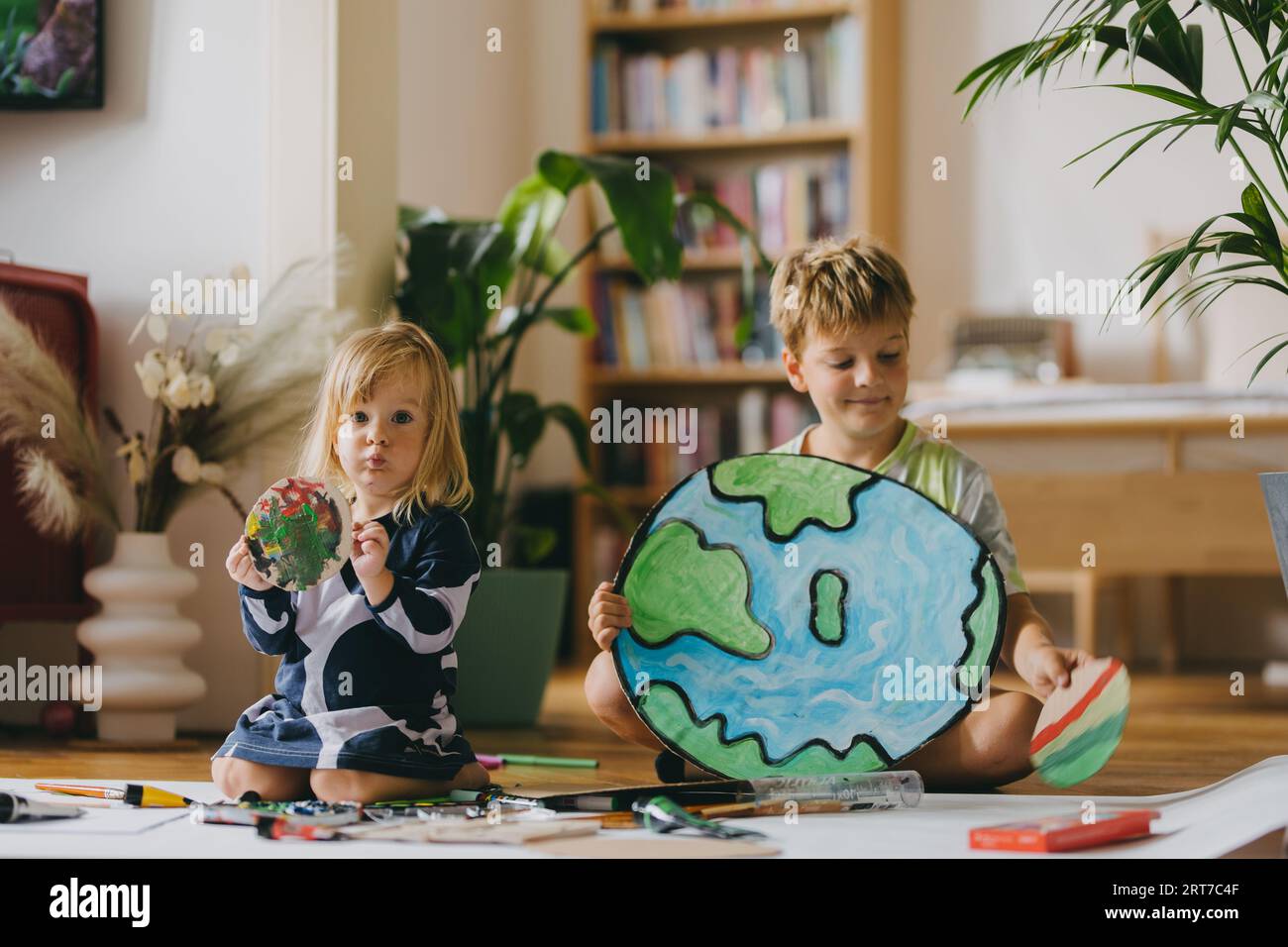 Siblings painting at home with watercolors and tempera paints, creating a model of planet Earth. Stock Photo