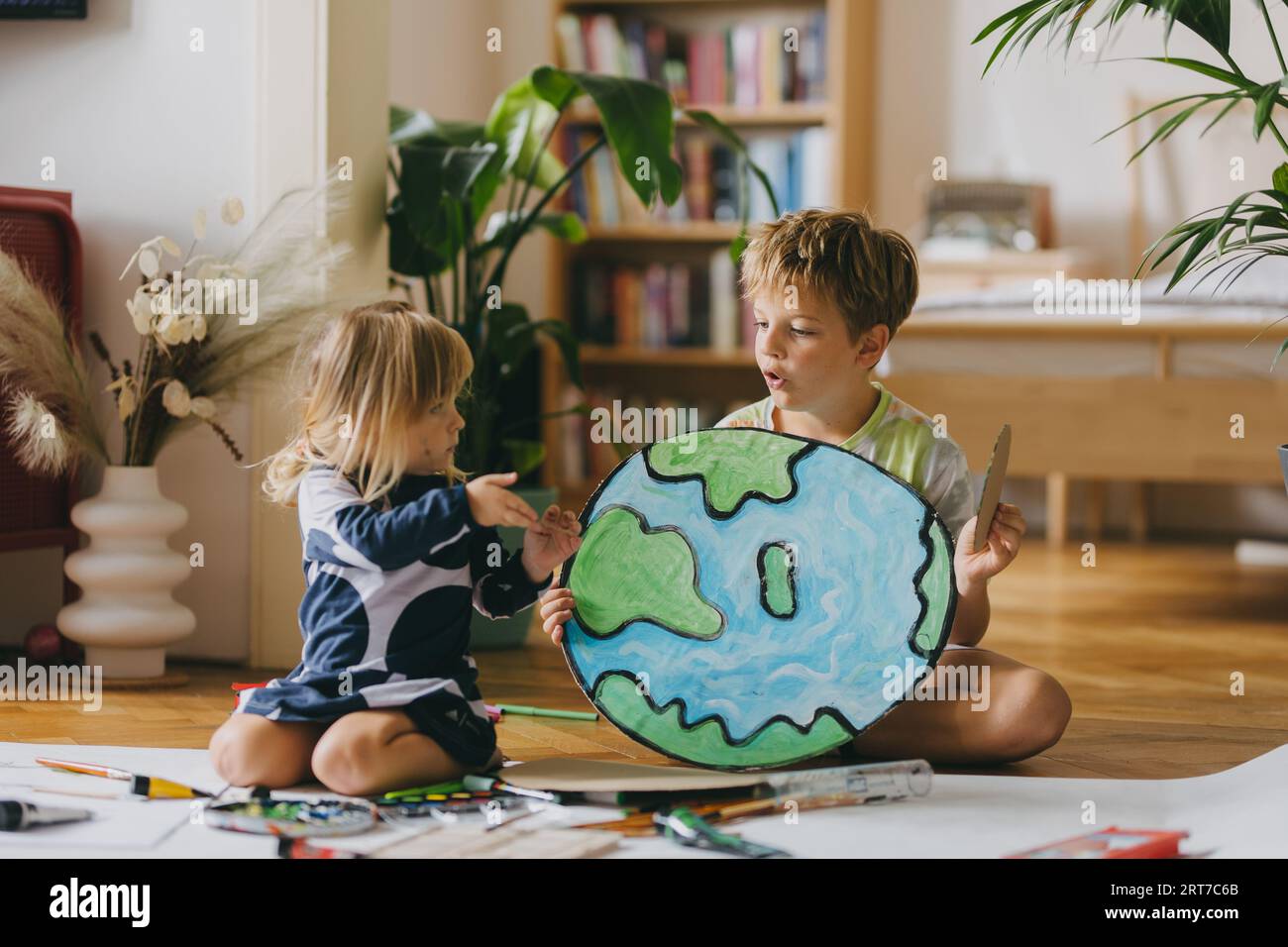 Siblings painting at home with watercolors and tempera paints, creating a model of planet Earth. Stock Photo