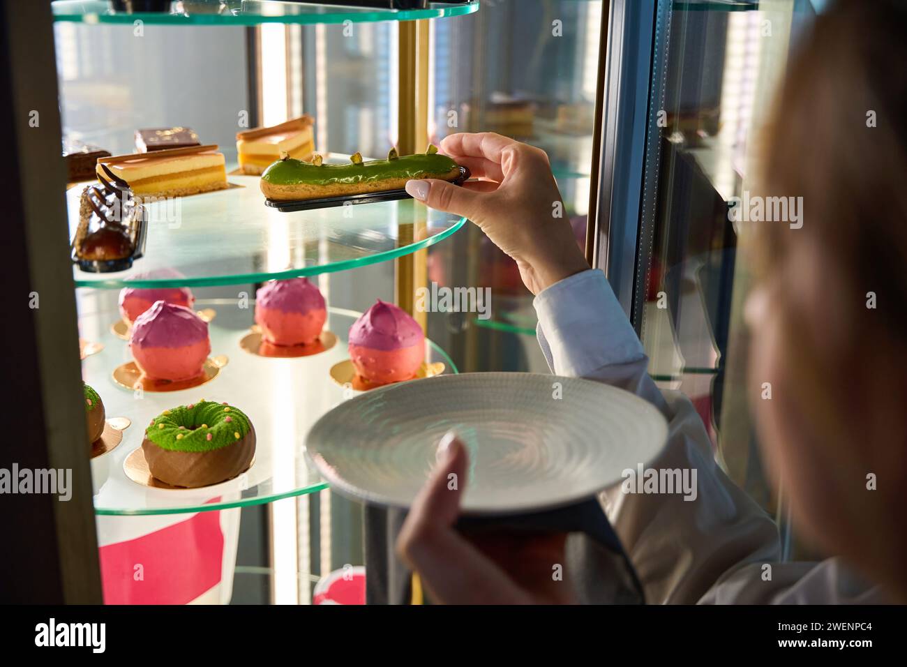 Woman takes out an eclair from a transparent display case Stock Photo