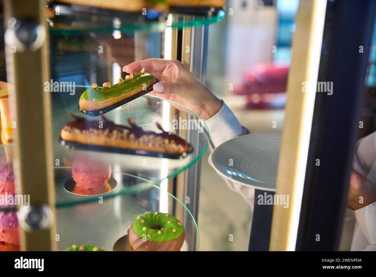 Waitress takes out an eclair from a transparent display case Stock Photo