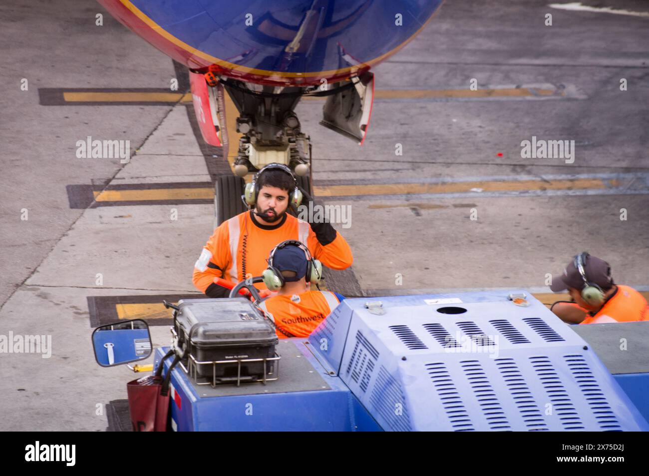 Miami, Florida, USA - 03 14 2024: A Southwest Airlines ground crew in orange uniforms operates an airport service vehicle under the nose of a blue Stock Photo