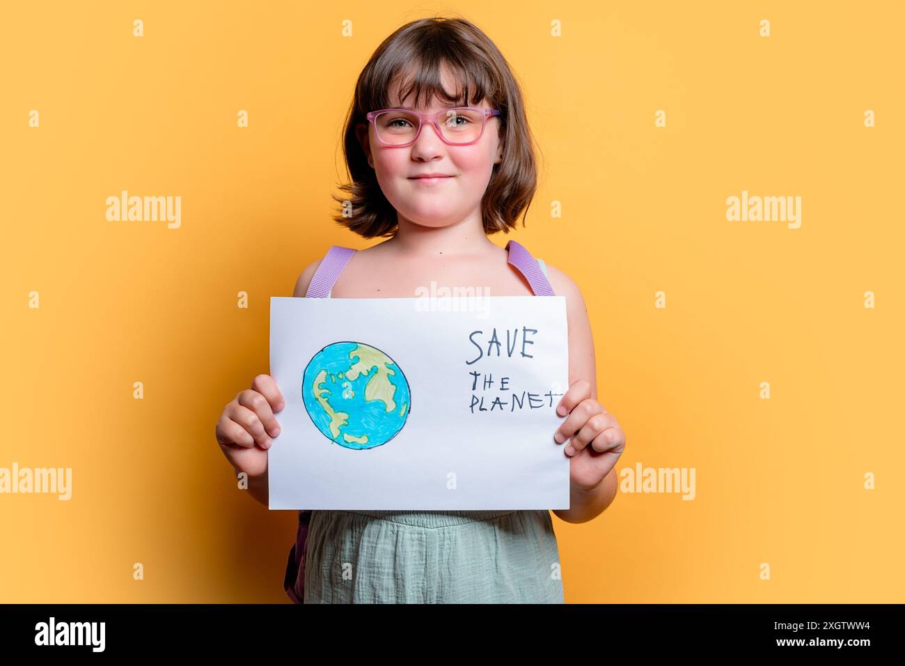 A young Caucasian girl confidently presents a handwritten Save the Planet sign, reflecting a strong environmental message Stock Photo