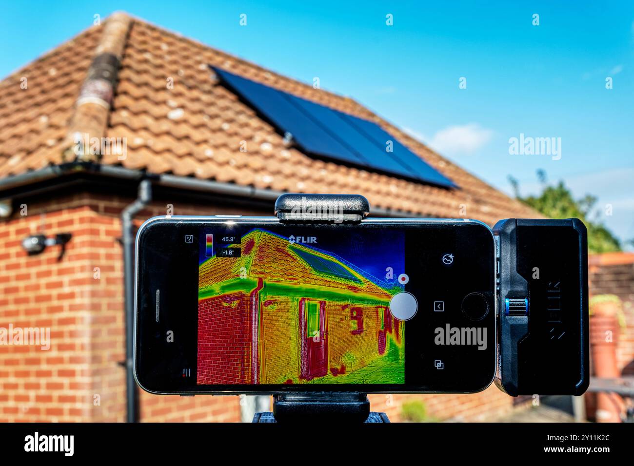 An infrared thermal imaging device being used to assess heat loss from a bungalow fitted with solar panels on the roof. Stock Photo