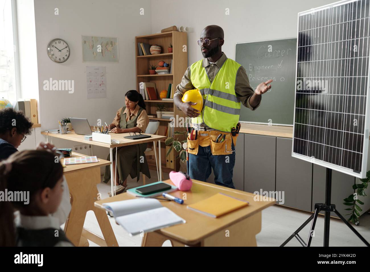 Young confident male technician or engineer in workwear standing in front of schoolkids and making presentation of solar panel Stock Photo