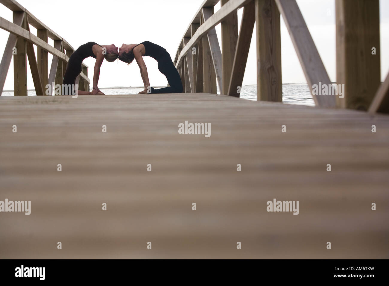 two women practise yoga poses on wood deck in nature Stock Photo