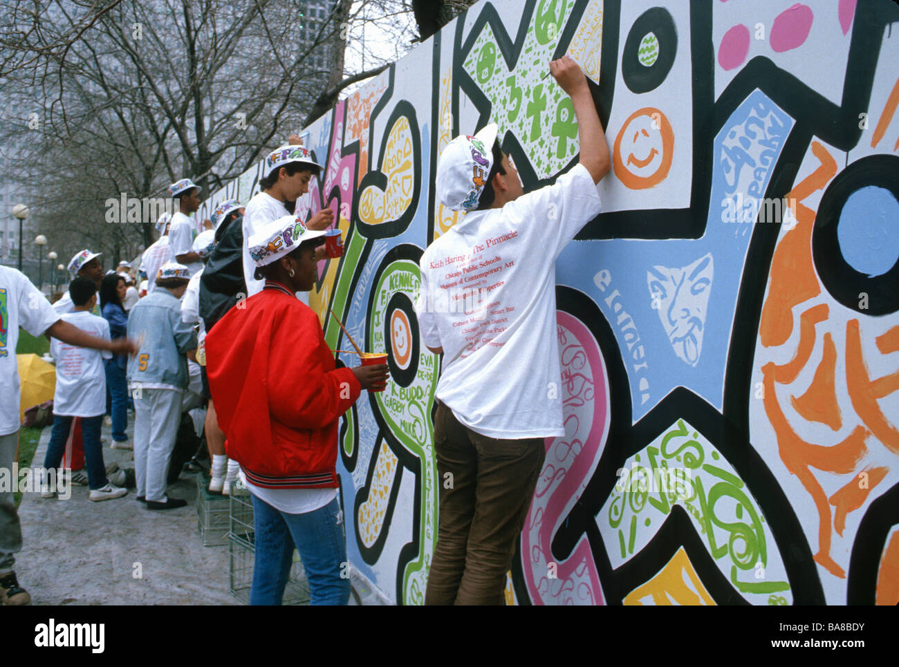 Teens in school art program paint in mural figures drawn by late artist Keith Haring in Grant Park Chicago Illinois Stock Photo