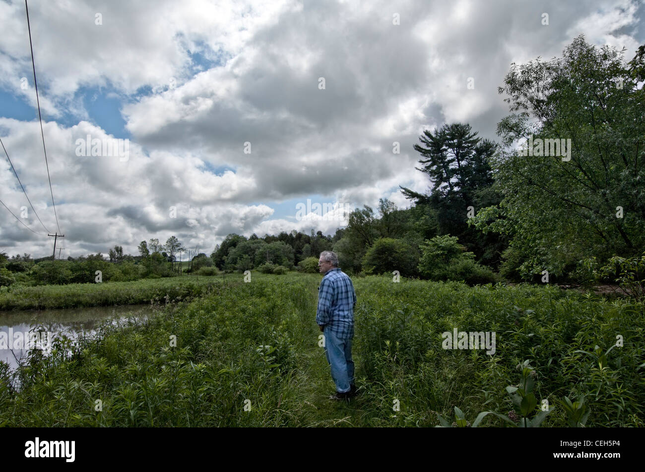 a man standing alone in a field near a pond Stock Photo