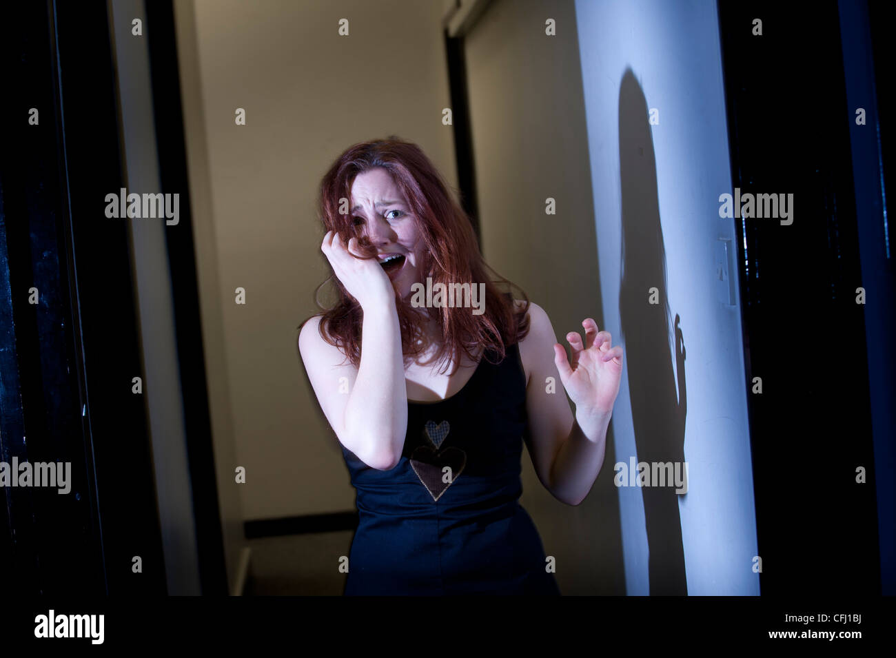 a single young red haired woman girl alone indoors scared afraid worried running away in fear Stock Photo